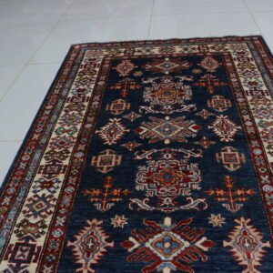 Handmade wool and cotton area rug or runner with traditional geometric Kazak pattern displayed on floor