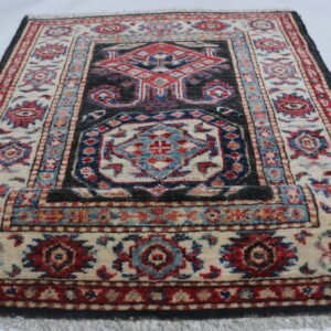 Handmade wool and cotton area rug or runner with traditional geometric Kazak pattern displayed on floor
